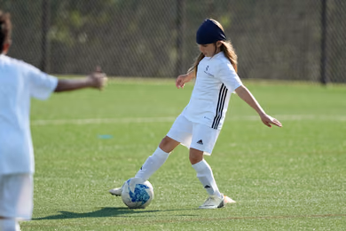 Young player in a blue beanie controlling a soccer ball on the grass at a Fundación Real Madrid camp